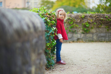 Adorable toddler girl in red poncho walking in autumn park