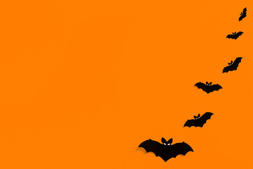 silhouettes of black paper bats on an orange background forming a frame, a flock of black bats on an orange background, Halloween concept, copy space. Flat lay for your design