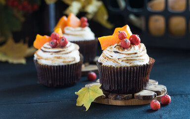 Homemade pumpkin muffins cupcakes decorated with meringue, berries and pieces of pumpkin on black wooden table. Selective focus, close-up