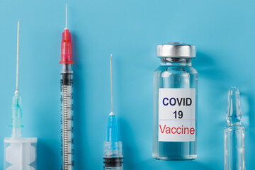 A set of ampoules with the inscription Covid-19 vaccine and a set of syringes against a blue background.