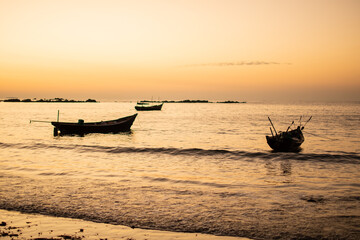 Three traditional wooden boats in a bright orange sunset, Ngwesaung, Myanmar