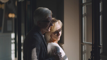 Mature smiling couple looking out through window indoors
