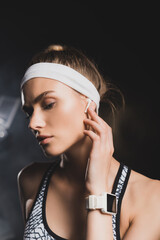 Portrait of sportswoman with smartwatch touching wireless earphone in gym