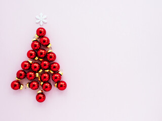Red Christmas toys in the form of a Christmas tree on a pink background, flatly, copyspace, top view