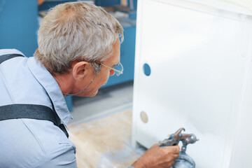 Painting of metal products. An elderly man paints a Cabinet with a compressor