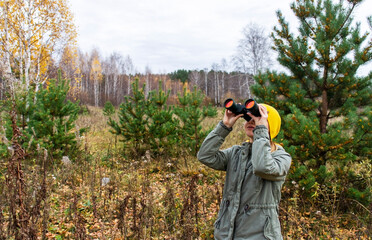 Fototapeta premium Young woman with binoculars watching birds in the autumn forest. Scientific research