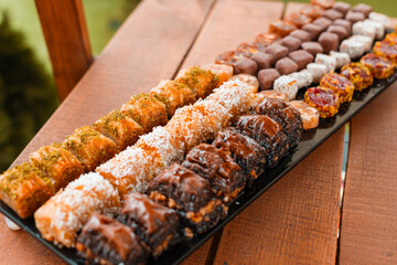 Diverse kinds of baklava on a black tray on a wooden table