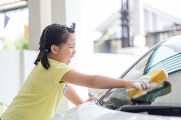 Car care with kid girl.6 years old asian child girl holding sponge with foam soap.washing car at home.Carwash service, Activity in family.Homeschool kid exercise.Lockdown during covid19 coronavirus.