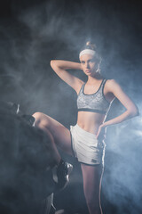 Obraz premium Selective focus of sportswoman looking at camera tear tire in sports center with smoke