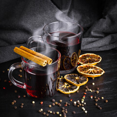 Two glass cups of mulled wine with steam over on dark table. Dried sliced citrus fruits and...