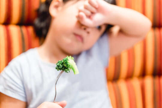 Little Asian Girl Make Vomiting Face When She Eat Broccoli Vegetable In Restaurant.Unhappy, Disgusted, Unlike Veggie Food.Little Asian Girl Child With No Appetite In Front Of The Meal.Bad Behavior.