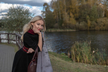 A beautiful lady stands and leans on the railing, with beautiful eyes in black clothes, in the fall against a background of blue clouds.