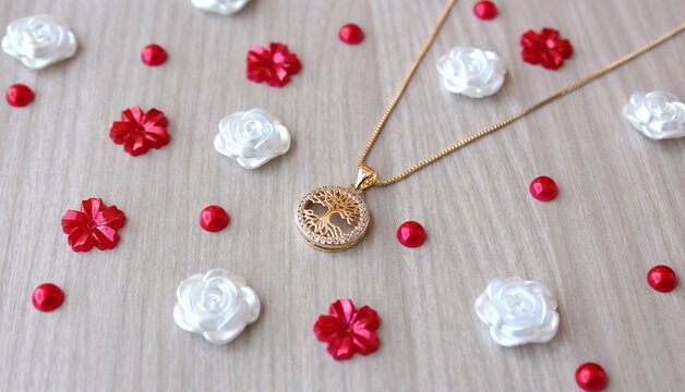 Colar gargantilha com pingente dourado cravejado de brilhantes. &Aacute;rvore da Vida, s&iacute;mbolo, acess&oacute;rio feminino, joia, fundo de madeira e flores brancas e vermelhas.