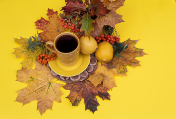 There is a cup of tea on a yellow background on autumn leaves. Lemons and rowan berries lie nearby..