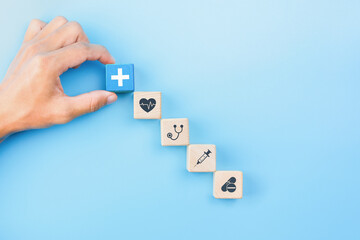 Health insurance concept, Hand holding wooden blocks with healthcare medical icons on blue background, copy space