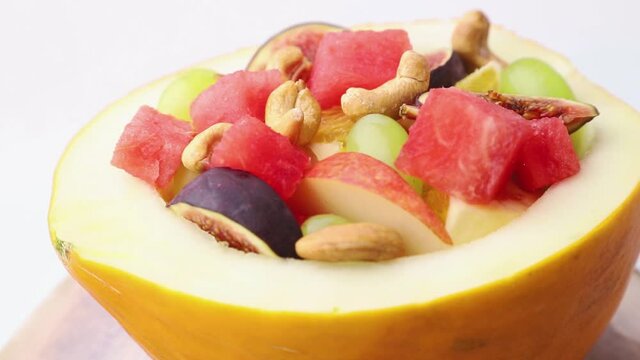 Rotating of vegetarian fruit salad of watermelon, grapes, figs, pear, orange on white background. Side view, close up.