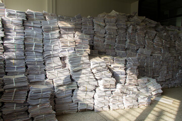 The used papers are tied and stacked together in a chamber to prepare for recycling. There was light from the sun through the windows, hitting a large pile of paper.