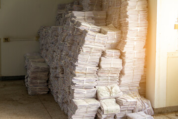 The used papers are tied and stacked together in a chamber to prepare for recycling. There was light from the sun through the windows, hitting a large pile of paper.