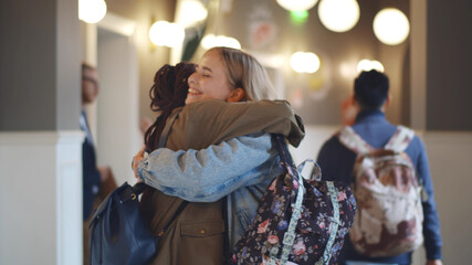 Two diverse female college classmates meeting and hugging in school corridor