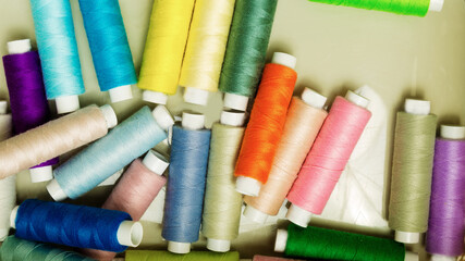 many multi-colored small spools with sewing thread on the light surface