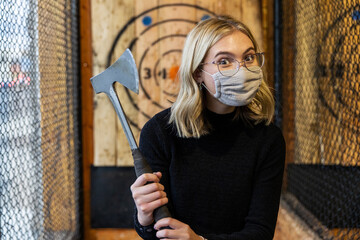 Teenage girl holds axe at an axe throwing range with target behind her - Powered by Adobe