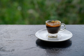shot espresso coffee in drinking glass on table with green view bokeh background
