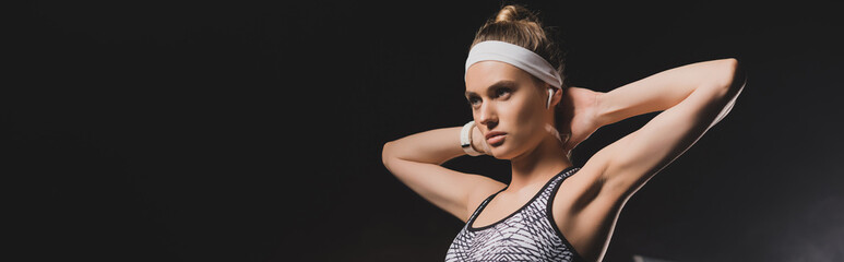 Panoramic shot of sportswoman with hands behind head on black background