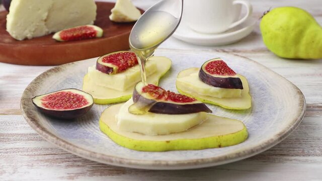 Summer appetizer with pear, cottage cheese, figs and honey on a white wooden background. Honey is pouring from a spoon. Side view, close up, selective focus.