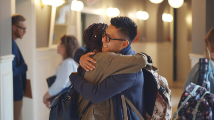 Happy multiethnic students embracing in university building corridor
