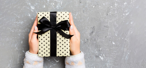 Girl Hands holding craft paper gift box with as a present for Christmas or other holiday on grey cement background, top view with copy sppace