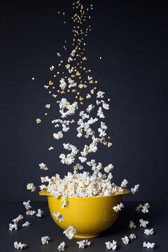 Popcorn falling into a yellow bowl on a black background. Transformation process