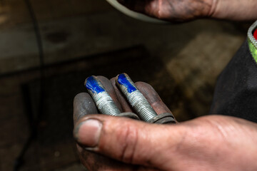 Car mechanic applies a layer of blue thread glue to the screw in his hand.