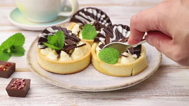 Sweet tartlets with chocolate and cheese cream cut with a spoon on white wooden background. Side view, close up.