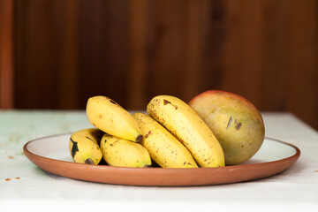 Fruits placed on a plate on the table. The fruits are bananas and mango. Textured wooden background in Brazilian cuisine. Copy space, top view. Food concept. Fruits concept.