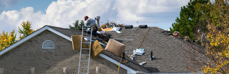 Worker on the roof of a 2-storey family house installing new asphalt shingles