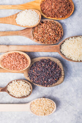 Organic white Jasmine rice, unpolished black and brown rice, Riceberry  in wooden spoons. White rice, Jasmine rice, Black rice, Brown rice, Riceberry and Mixed rice in wooden spoon over black table ba