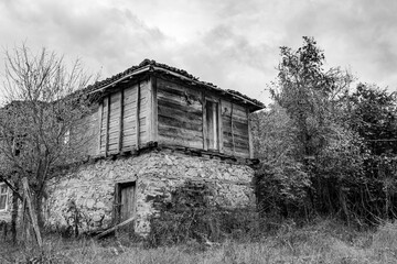 Black and white travel photograph, partial view of abandoned old house, rural landscape, Strandzha mountain, Bulgaria, wooden planks facade.