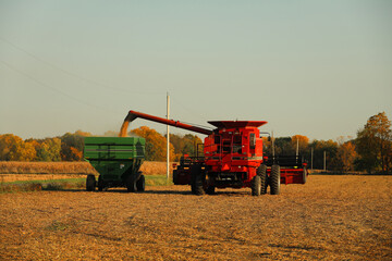 Red combine unloading soybeans into green grain wagon; copy space - Midwest, USA

