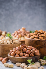 Obraz na płótnie Canvas Assortment of nuts in a wooden bowls, on a gray background. Hazelnuts, pistachios, almonds, brazil nut, cashews