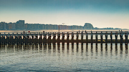 Nieuwpoort's mole with tourists walking on it by the river Yser with the beach and the city in the background.