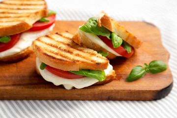 Tasty Grilled Caprese Panini (Mozzarella, Tomatoes and Basil) on a rustic wooden board, side view. Close-up.