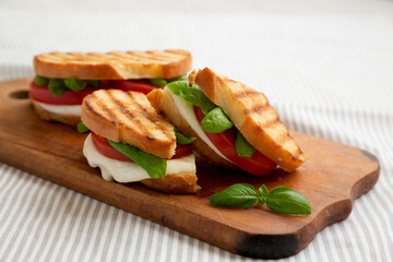 Tasty Grilled Caprese Panini (Mozzarella, Tomatoes and Basil) on a rustic wooden board, low angle view. Close-up.