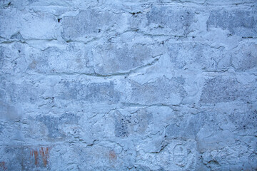 The old gray brick wall is poorly painted with white paint.