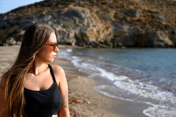 Mujer paseando por la orilla de la playa con ropa negra y gafas de sol