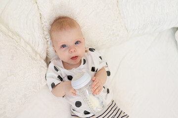 baby 8 months old lying on the bed in pajamas and drinking milk from a bottle, baby food concept,...
