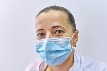 Close up head of tired female doctor in mask, mature woman looking at camera