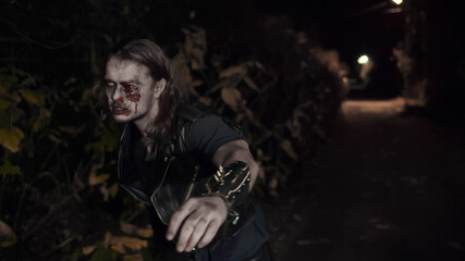 Fototapeta na wymiar Angry zombie man with bloody face walking along night road