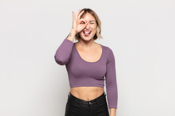 young pretty woman smiling happily with funny face, joking and looking through peephole, spying on...