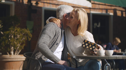 Senior man giving nice present to wife sitting together on restaurant terrace