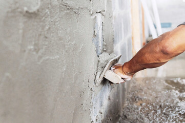 closeup hand of worker plastering cement at wall in construction site